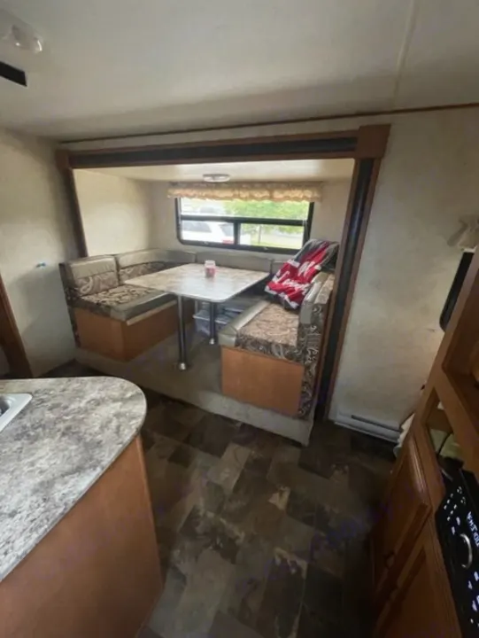 Interior of an RV rental featuring a dinette with patterned cushions, a sturdy table, kitchen counter, and a view outside.. Coachmen Apex 2013