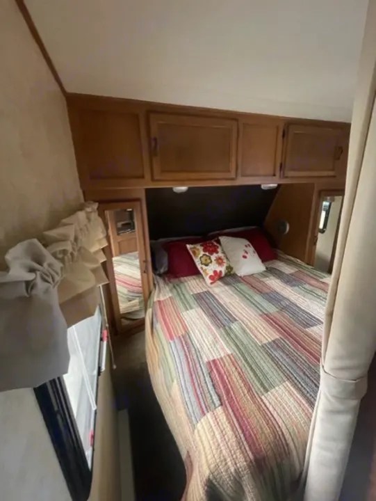 Cozy RV rental bedroom with a colorful quilt on the bed and wooden cabinets overhead. Perfect for your next adventure.. Coachmen Apex 2013