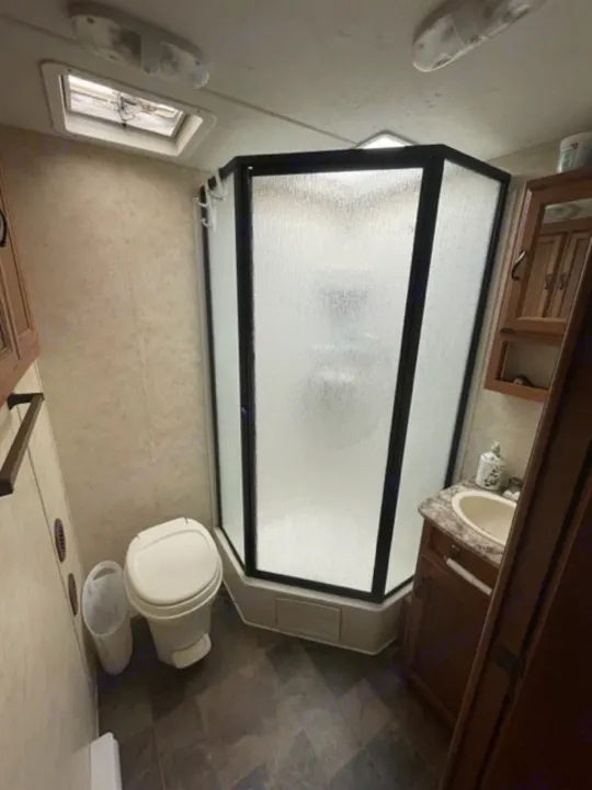 Compact RV rental bathroom with shower, toilet, and sink. Designed for efficient use of space.. Coachmen Apex 2013
