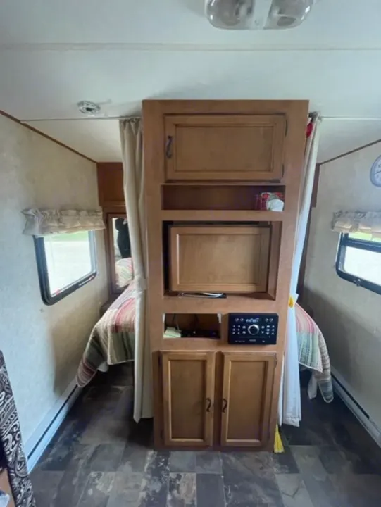 Explore this RV rental's clever interior: a central wooden unit with storage and stereo, flanked by colorful beds & windows.. Coachmen Apex 2013