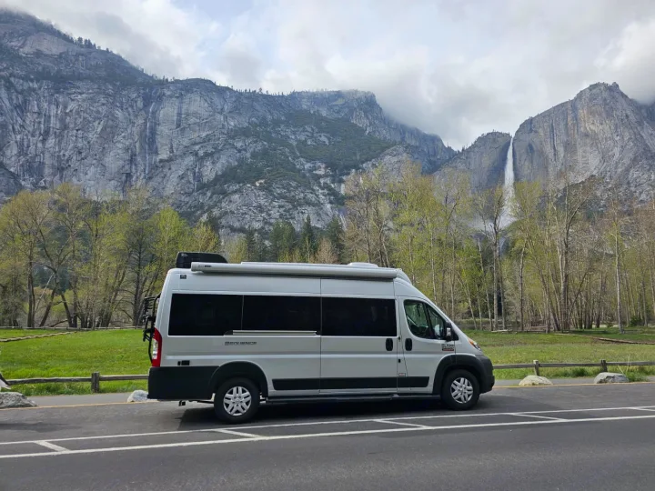 Explore stunning nature! This rv rental, a light gray camper van, is parked with Yosemite Falls and towering granite cliffs as a backdrop.. Thor Motor Coach Sequence 2022