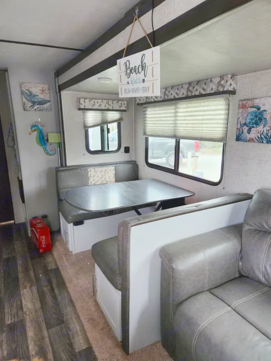 RV rental interior showcasing a grey dinette with a dark table, a plush couch, and beach-themed decor. Features carpet and wood-look flooring.. Keystone RV Bullet Ultra Lite 2020