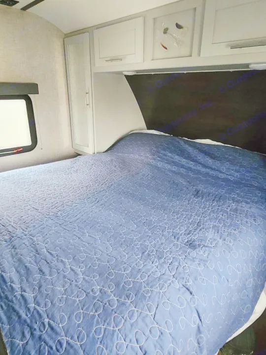 Cozy RV rental bedroom with a large bed, blue quilt, white cabinets, and a window, perfect for comfortable travel.. Keystone RV Bullet Ultra Lite 2020