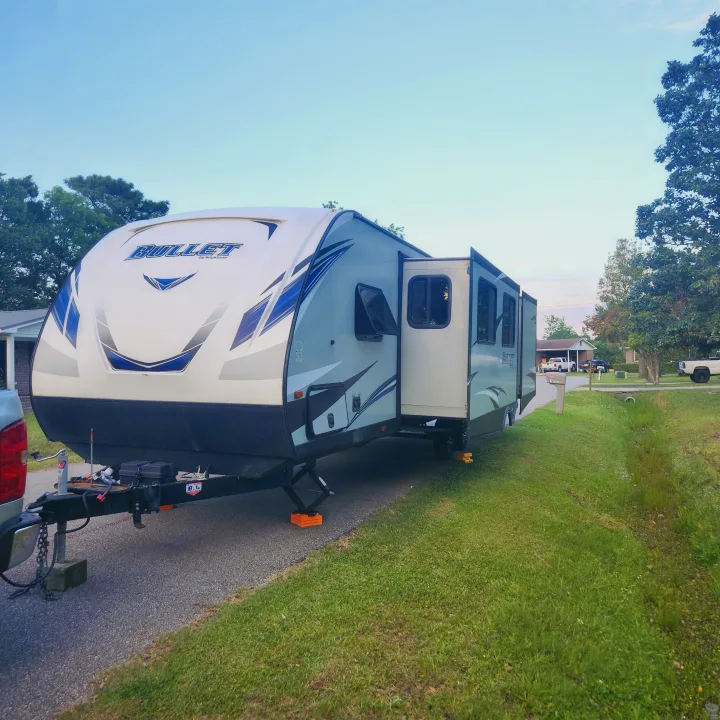 Bullet travel trailer, perfect for an RV rental getaway, parked and stabilized on a paved driveway with slide-out extended.. Keystone RV Bullet Ultra Lite 2020