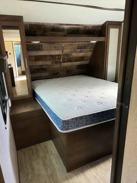 Cozy RV rental bedroom: a comfy bed with white mattress, dark wood headboard, and built-in storage with a mirror.. Aspen Trail Aspen Trail Trailer 2021
