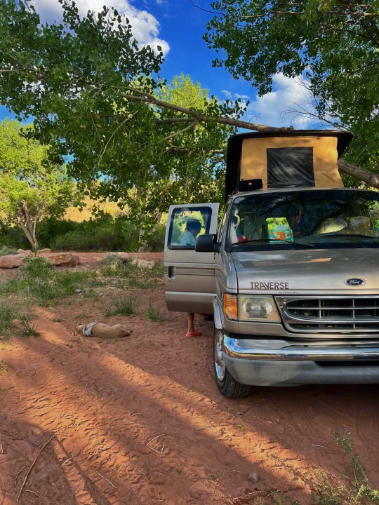 A Ford Traverse camper van (RV rental) under trees, dog naps on red earth. Ideal van life camping adventure.. Ford Pleasure Way Xl Rd Widebody 2002