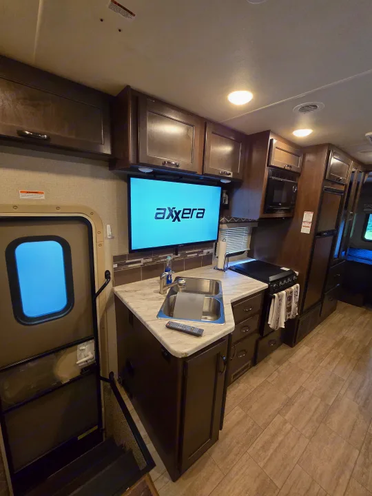 RV rental interior showcasing a compact kitchen with sink, stove, microwave, and TV. Ideal for comfortable road trips.. Thor Freedom Traveler 2020