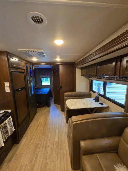 Spacious RV rental interior featuring a kitchen, dinette, and visible bedroom beyond, all with light wood-look flooring.. Thor Freedom Traveler 2020