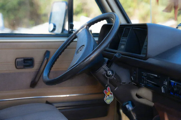 Inside an RV rental: a vintage steering wheel, dashboard, and a unique peace sign keychain. Ready for adventure!. Volkswagen T3 Westfalia 1985