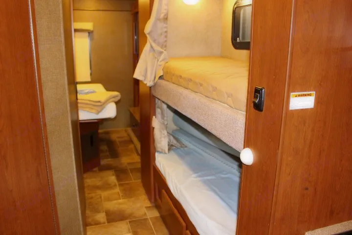 This rv rental features built-in bunk beds on the right, and a bed further down the hallway, offering multiple sleeping areas.. Thor Chateau 2016