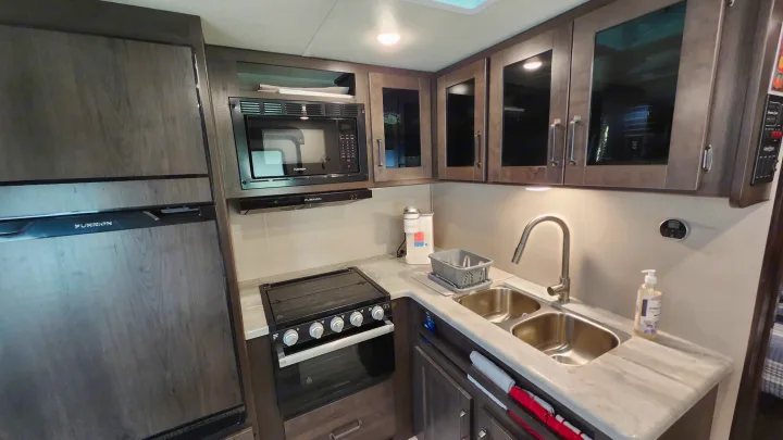 Modern RV rental kitchen with a large refrigerator, microwave, oven/stove, and double sink.. Grand Design Transcend Xplor 2022