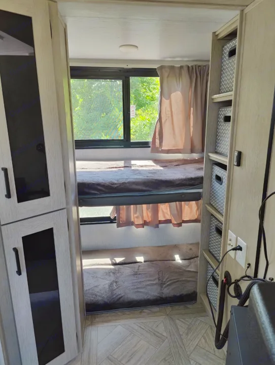 Cozy RV rental interior showing two bunk beds with blankets, a window view, and built-in storage.. Forest River Salem Cruise Lite 2024