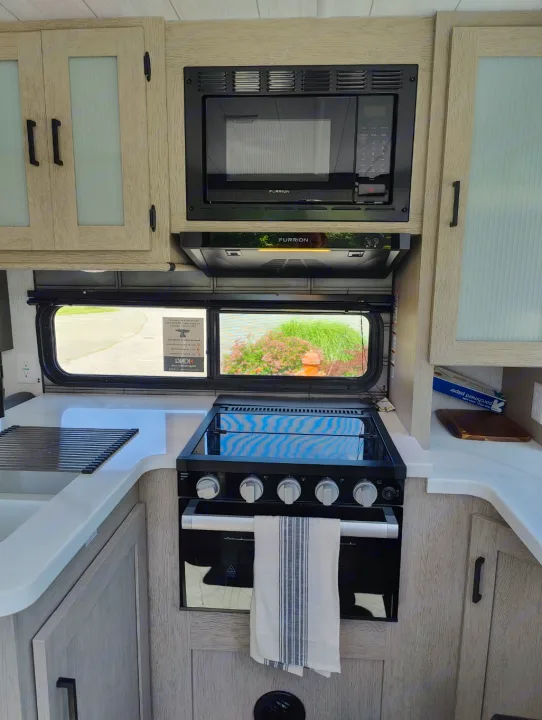 RV rental kitchen view: Modern design with microwave, gas stove, oven, and sink. Light wood cabinets and white counters.. Forest River Salem Cruise Lite 2024