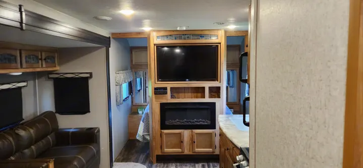 An RV rental's inviting interior: living area with sofa, entertainment center (TV & fireplace), and glimpse of kitchen.. Coachmen Freedom Express 2019
