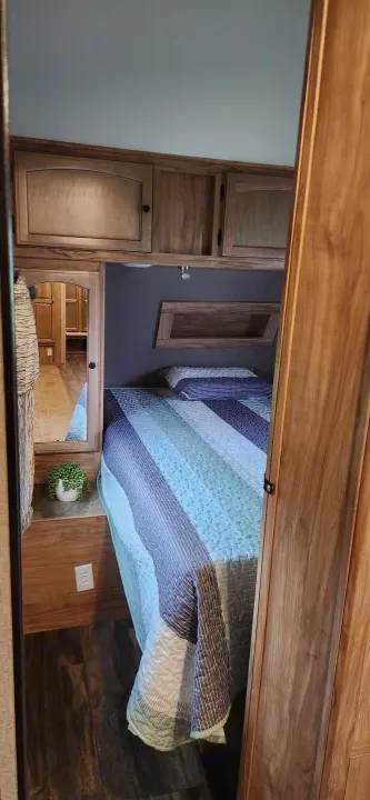 Cozy RV rental bedroom featuring wood cabinetry, a comfortable bed with a striped quilt, and a convenient mirror.. Coachmen Freedom Express 2019