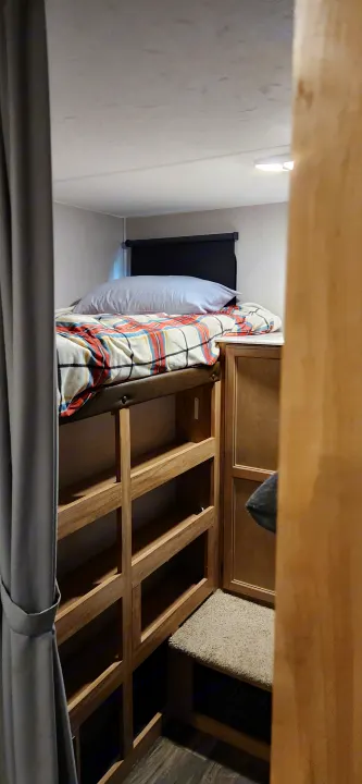 Compact RV rental bunk bed with a plaid blanket, built-in wooden storage shelves, and a carpeted step.. Coachmen Freedom Express 2019