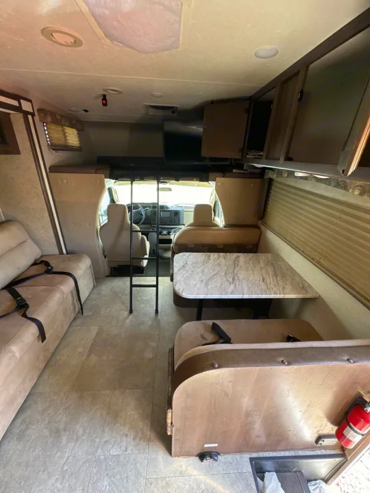 Spacious RV rental interior with dinette, sofa, and overhead bunk. Cockpit visible ahead for travel.. Coachmen Freelancer 2019