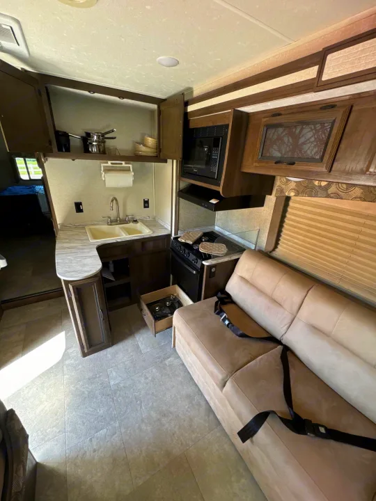 RV rental interior: cozy kitchen with sink, stove, microwave & living area sofa with seatbelts. Perfect for travel.. Coachmen Freelancer 2019