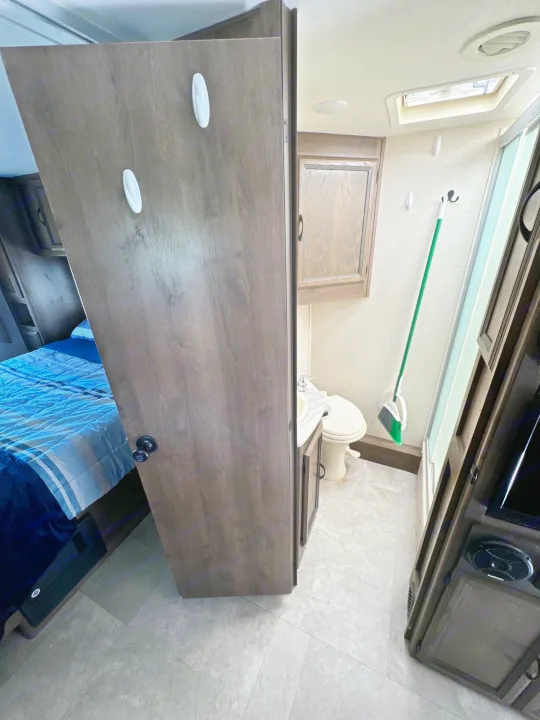 RV rental interior: a space-saving design revealing a bedroom entrance, and a compact bathroom with toilet, sink, & shower.. Coachmen Freelancer 2019