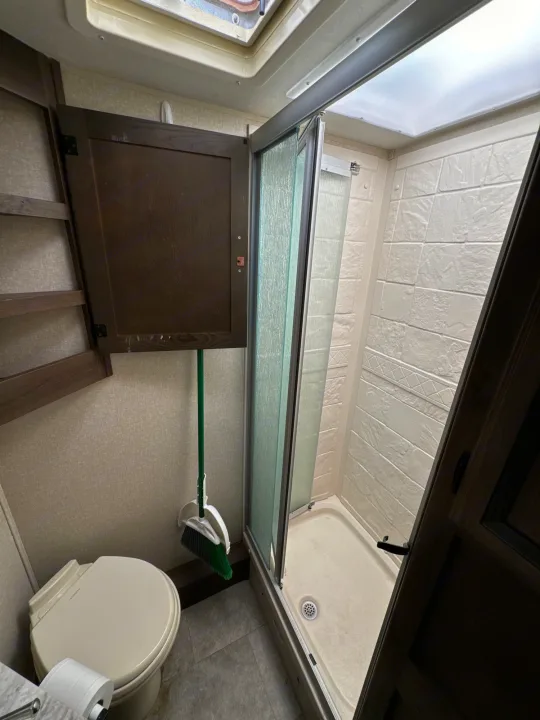 Inside an RV rental: a compact bathroom featuring a toilet, shower, and broom hanging from cabinetry.. Coachmen Freelancer 2019