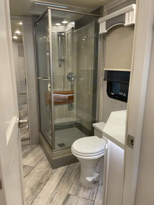 Modern RV rental bathroom featuring a spacious glass shower, toilet, and stylish grey interior.. Fleetwood Discovery 2021
