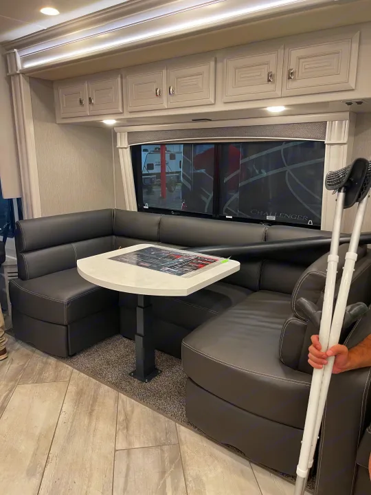 Inside an RV rental: L-shaped dinette with dark seating, white table, and overhead cabinets. Spacious layout for travel.. Fleetwood Discovery 2021
