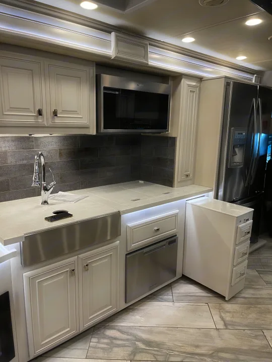 RV rental kitchen: modern white cabinets, stainless appliances, pull-out storage, and illuminated counters.. Fleetwood Discovery 2021