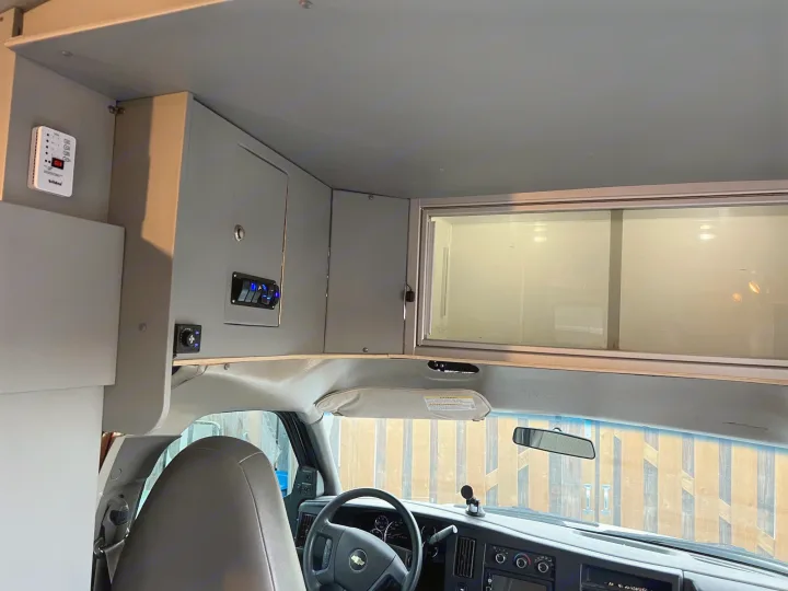 RV rental interior view towards the front. Overhead cabinets, thermostat, stereo, and driver's dashboard with steering wheel are visible.. Chevrolet Express shuttle 2014