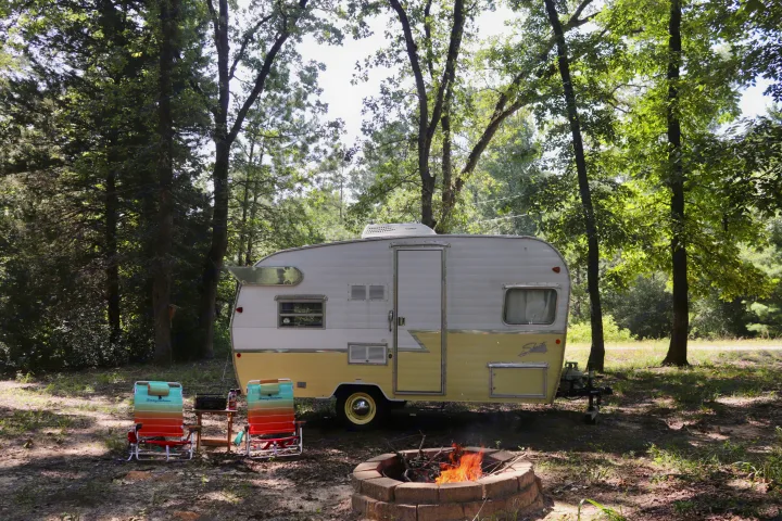 Vintage rv rental parked at a serene campsite with a cozy campfire and chairs. Perfect for outdoor escapes.. Shasta Airflyte 2016