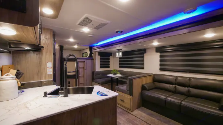 Modern rv rental interior featuring a kitchen, U-shaped dining booth, and sofa with striking blue accent lighting.. Forest River Cherokee Alpha Wolf 2021