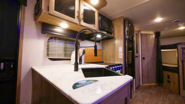Modern kitchen in an RV rental with white countertops, sink, microwave, stove, and refrigerator for comfortable road trips.. Forest River Cherokee Alpha Wolf 2021