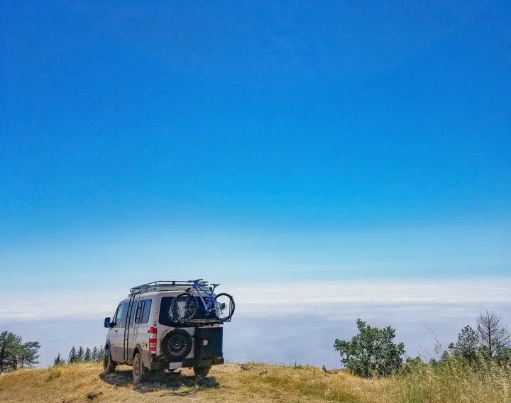 RV rental van with bike parked on a mountain, overlooking a vast sea of clouds under a clear blue sky. Adventure awaits!. Sportsmobile Regular Body 4X4 2017