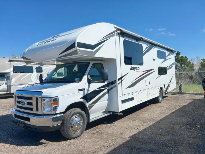 Front-side view of a white Jayco Redhawk Class C RV rental parked on a gravel lot under a clear blue sky.. Redhawk 31F MC 2019