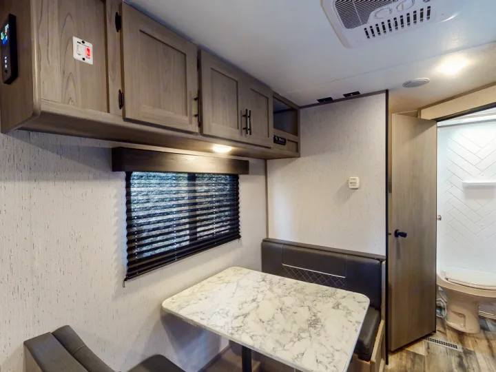 Bright RV rental interior: dinette with table & bench seating, overhead cabinets, plus an accessible bathroom.. Coleman Lantern LT 274BH 2024