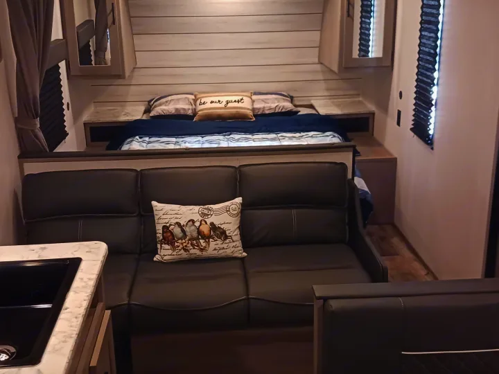 Cozy RV rental interior: bed, sofa with bird pillow, and kitchen. Ready for your adventure!. Coleman Lantern LT 274BH 2024