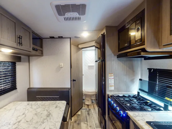 Comfortable RV rental interior showcasing a kitchen with stove and microwave, a dinette, and a visible bathroom.. Coleman Lantern LT 274BH 2024