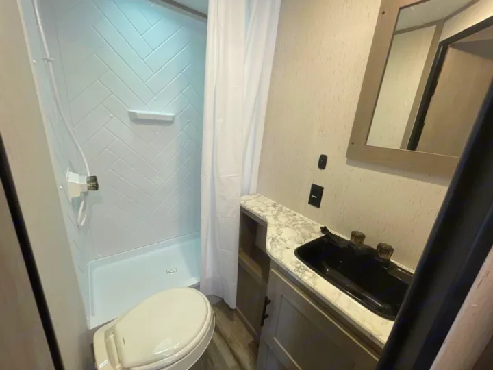 RV rental bathroom: modern white shower, toilet, vanity with black sink, and mirror.. Coleman Lantern LT 274BH 2024
