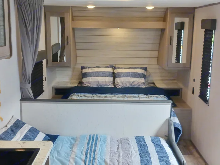 Inside an RV rental: a comfortable bedroom with striped bedding, bunk, overhead cabinets, and soft lighting.. Coleman Lantern LT 274BH 2024