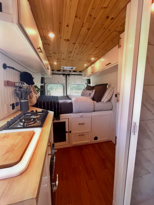 Bright and modern RV rental interior featuring a cozy bed, functional kitchen area, and clever storage solutions.. Dodge B Van 2015