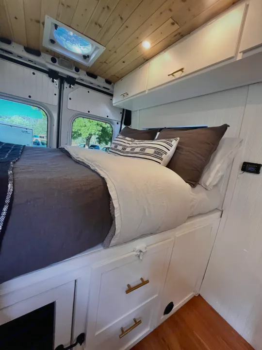 Inviting RV rental camper van interior. Features a cozy bed, white storage cabinets, and a warm wood ceiling.. Dodge B Van 2015