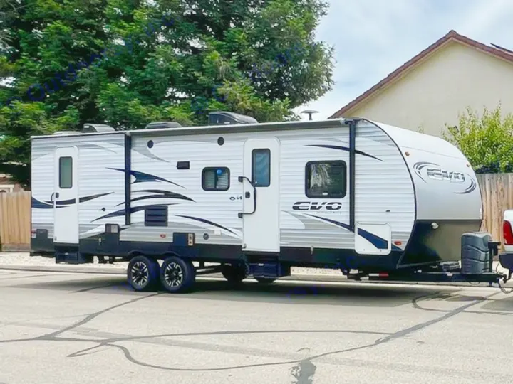 A long, white and black EVO travel trailer, ideal for RV rental getaways. It's parked on a paved street, promising outdoor recreation.. Forest River Evo 2017