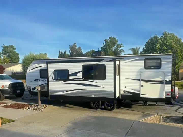 A long white and grey EVO travel trailer, an RV rental, is parked outdoors with its slide-out extended.. Forest River Evo 2017