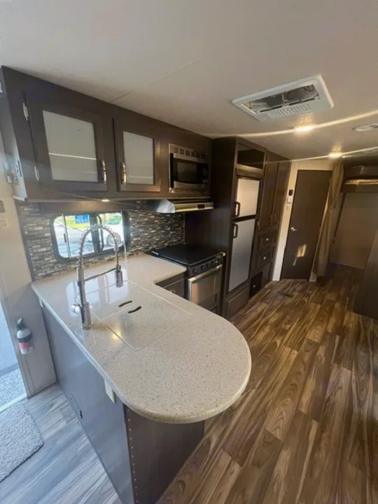 This RV rental boasts a full kitchen with dark cabinets, a peninsula counter with sink, microwave, fridge, and wood floors.. Forest River Evo 2017
