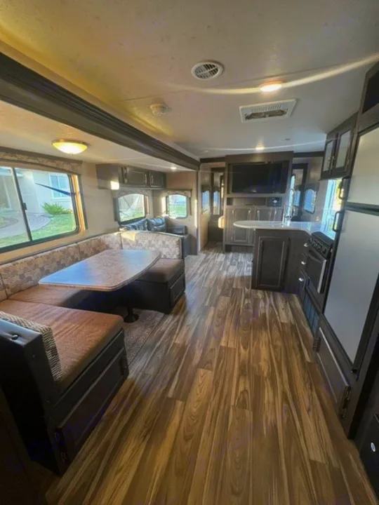 Spacious RV rental interior featuring modern wood flooring, a U-shaped dinette, full kitchen, and entertainment center.. Forest River Evo 2017