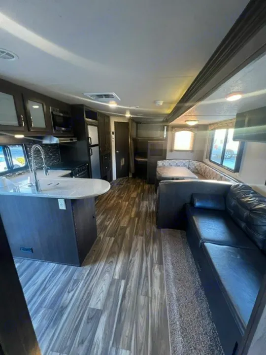Inside a modern RV rental: full kitchen with island, living area, and dining booth with wood-look flooring.. Forest River Evo 2017