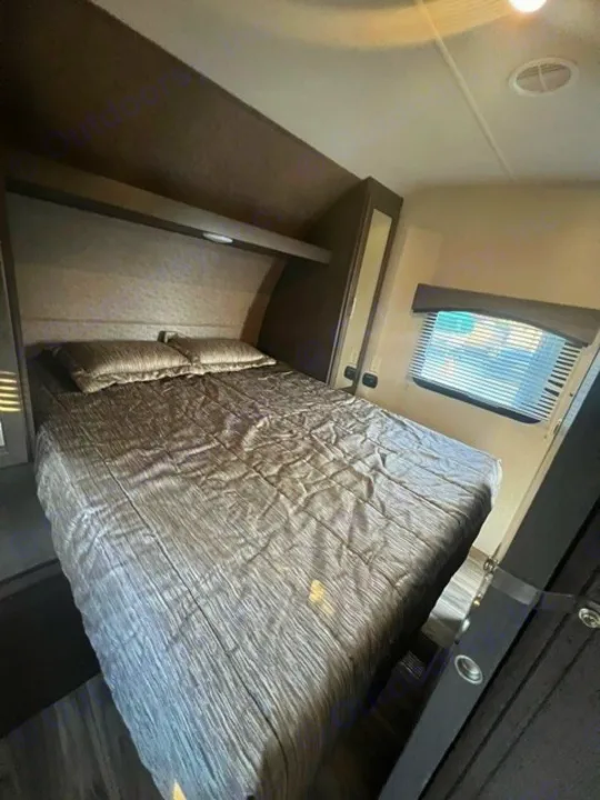 Cozy RV rental bedroom featuring a comfortable bed, overhead storage, and window blinds. Ideal for travel comfort.. Forest River Evo 2017
