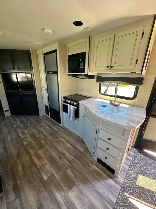 Inside a bright RV rental: a modern kitchen with a stove, microwave, fridge, and stylish wood-look flooring and cabinets.. Highland Ridge RV Open Range 2022