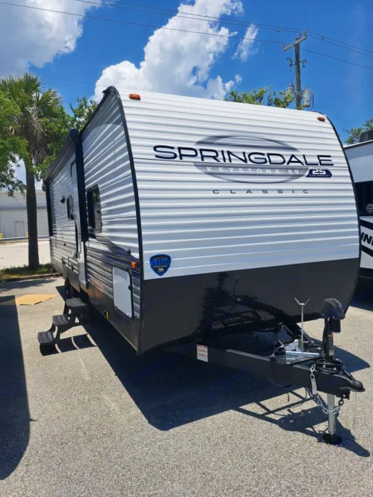 This white and black Springdale Keystone RV Classic travel trailer, ideal for rv rental, is parked outdoors with steps deployed.. Keystone RV SG261BHC 2024