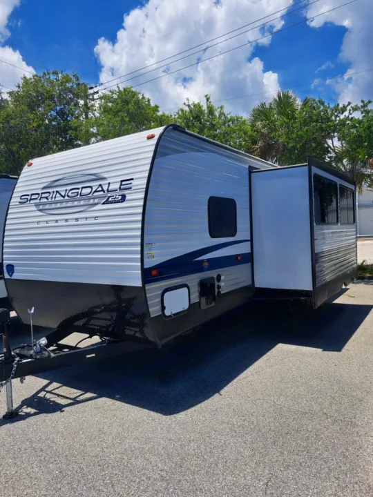 White and blue Springdale travel trailer RV rental, parked with slide-out extended for your next camping adventure.. Keystone RV SG261BHC 2024