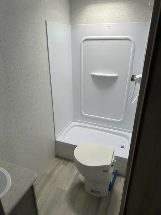 Explore this compact RV rental bathroom, featuring a white shower with an integrated toilet, and a small sink area.. Keystone RV SG261BHC 2024